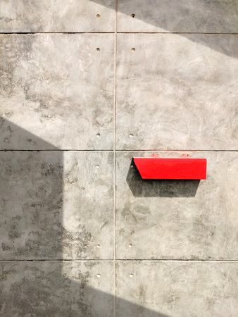 Red postbox on the old bare concrete wall in vintage loft style with sunlight and shadow on surface, front view and vertical frameの写真素材