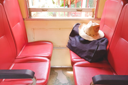 A straw hat and travel bag placed on red train seats near a window, symbolizing adventure, freedom,...