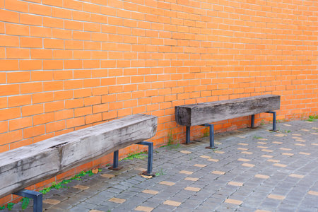 Minimal outdoor wooden long benches against curve brick wall, rustic wood seats with metal legs on...
