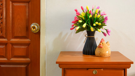 Interior home decoration with colorful artificial flowers in black vase and ceramic chicken on wooden cabinet near door in vintage houseの写真素材
