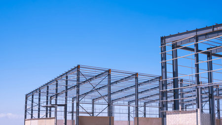 Metal structure of 2 industrial warehouse factory buildings framework in construction site against...