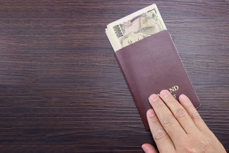 Man's hand holding international passport and Japanese money on brown dark wooden table.