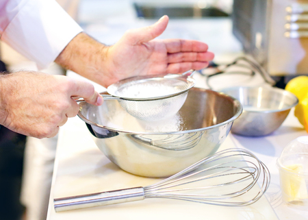 Baker sieving flour into a bowl in the kitchen of the bakeryの写真素材