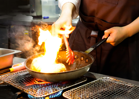 Chef cooking with flame in a frying pan on a kitchen stove, Chef in restaurant kitchen at stove with panの写真素材