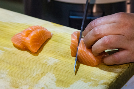 Hands cutting salmon fish on wooden board, Salmon sliced for nigiri sushiの写真素材