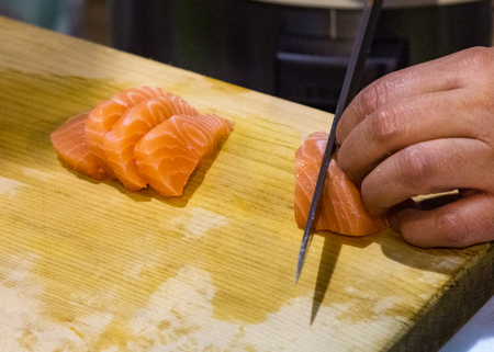 Hands cutting salmon fish on wooden board, Salmon sliced for nigiri sushiの写真素材