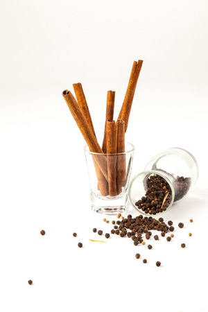 cinnamon and black pepper seeds in a glass, Black pepper is scattered on a white background from glass bottleの写真素材