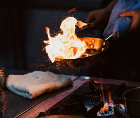 Chef cooking with flame in a frying pan on a kitchen stoveの写真素材