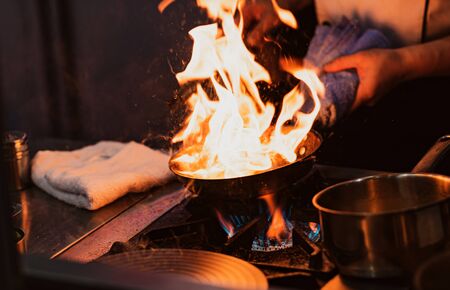 Chef cooking with flame in a frying pan on a kitchen stoveの写真素材