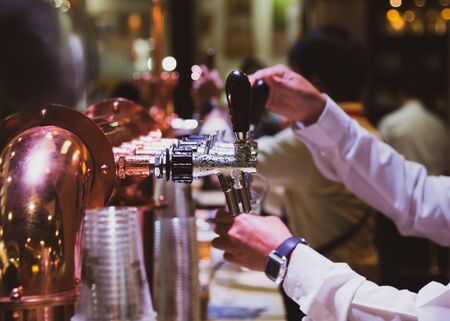 Bartender pouring draft beer in the bar, Barman hand at beer tap pouring draught lager beer serving in a restaurant or pubの写真素材