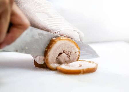 Chef in restaurant kitchen cutting meat, chef hands slicing belly pork rolled jointの写真素材