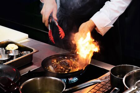 Chef cooking with flame in a frying pan on a kitchen stove
の写真素材