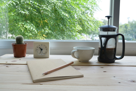 notebook with pencil and coffee pot on wooden tableの写真素材