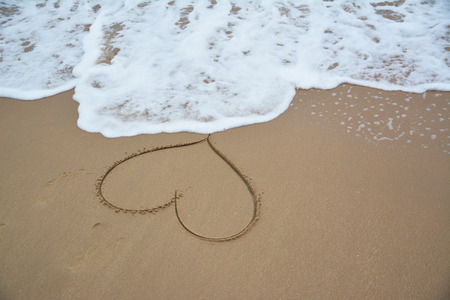 Draw a heart on the beach with waves.の写真素材