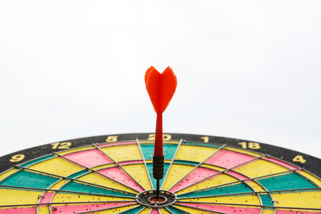 Red dart arrow on center of dartboard isolated on white backgroundの写真素材