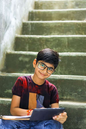 Indian / Asian Little boy studying online using mobile phone at homeの写真素材