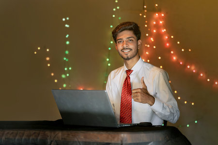 Young indian man working on laptop at home over lighting background