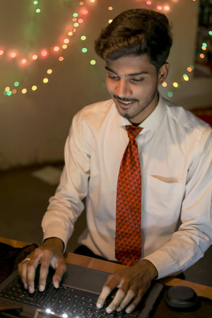 Young indian man working on laptop at home over lighting background