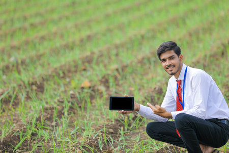 Young indian agronomist showing smart phone at agriculture fieldの写真素材