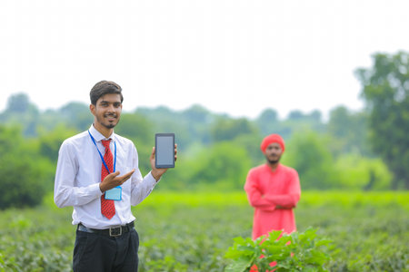 Young indian agronomist showing smart phone with farmer at green chilly fieldの写真素材