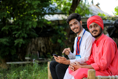 Young indian agronomist or banker showing some information to farmer in smart phoneの写真素材