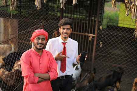 Indian banker or animal husbandry officer showing smart phone with farmer at goat dairy farmの写真素材