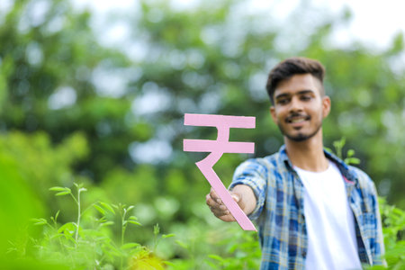 Young indian man holding indian rupees symbol in hand over nature backgroundの写真素材