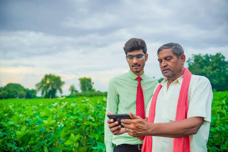 Young indian agronomist Discussing with farmer and showing some information in tabletの写真素材