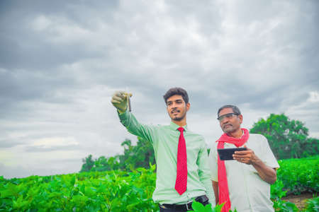 young indian handsome agronomist and farmer analyzing with test tube and tablet in fieldの写真素材