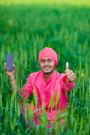 Young indian farmer showing smartphone screen in wheat fieldの写真素材