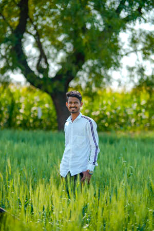 Young indian man standing at green wheat field