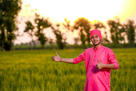 Young indian farmer standing at green wheat field
