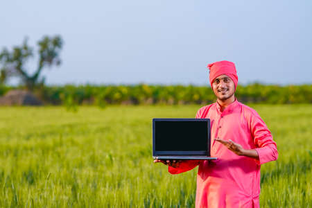 Young indian farmer showing laptop screen at wheat fieldの写真素材
