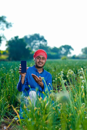 Young indian farmer showing smartphone screen at agriculture field