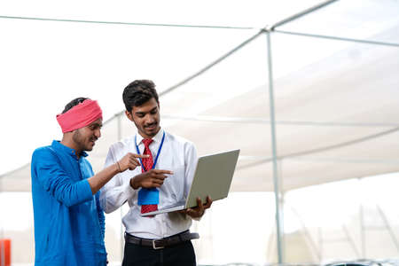 Young indian agronomist showing some information to farmer in laptop at greenhouseの写真素材