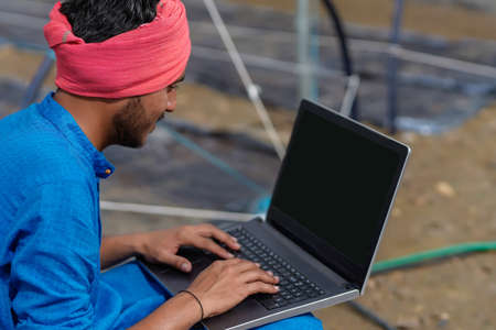 Young indian farmer using laptop at greenhouse or poly houseの写真素材