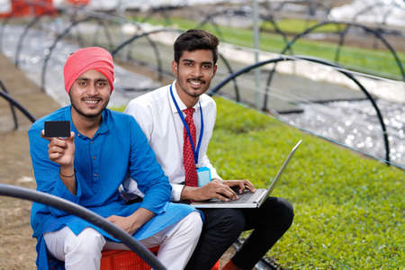Young indian agronomist showing some information to farmer in laptop at greenhouseの写真素材