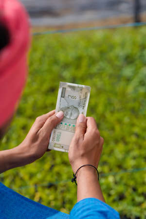 Young indian farmer counting and showing money at greenhouseの写真素材