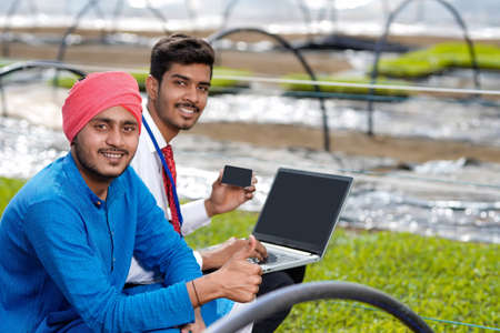 Young indian agronomist showing some information to farmer in laptop at greenhouseの写真素材