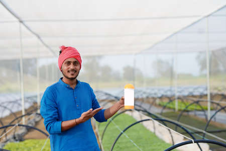 Young indian farmer showing fertilizer bottle at greenhouse