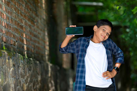 childhood, technology and people concept - indian cute school boy showing smartphone with blank screenの写真素材