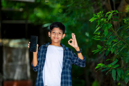 childhood, technology and people concept - indian cute school boy showing smartphone with blank screenの写真素材