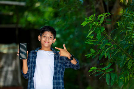 childhood, technology and people concept - indian cute school boy showing smartphone with blank screenの写真素材