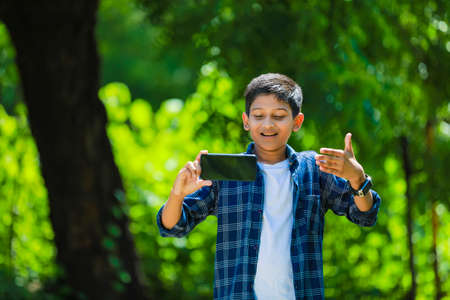 childhood, technology and people concept - indian cute school boy showing smartphone with blank screenの写真素材