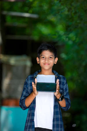 technology and people concept - smiling teenage boy in blue shirt showing smartphone with blank screenの写真素材