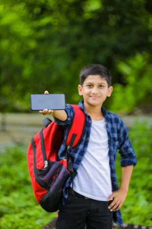 technology concept: Cute indian little school boy holding bag and showing smartphoneの写真素材
