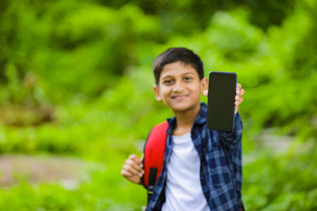 technology concept: Cute indian little school boy holding bag and showing smartphone
