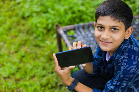 technology and people concept - smiling teenage boy in blue shirt using smartphone