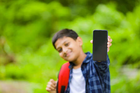 technology concept: Cute indian little school boy holding bag and showing smartphoneの写真素材