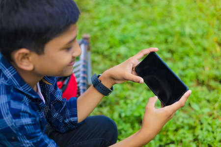 technology and people concept - smiling teenage boy in blue shirt using smartphoneの写真素材